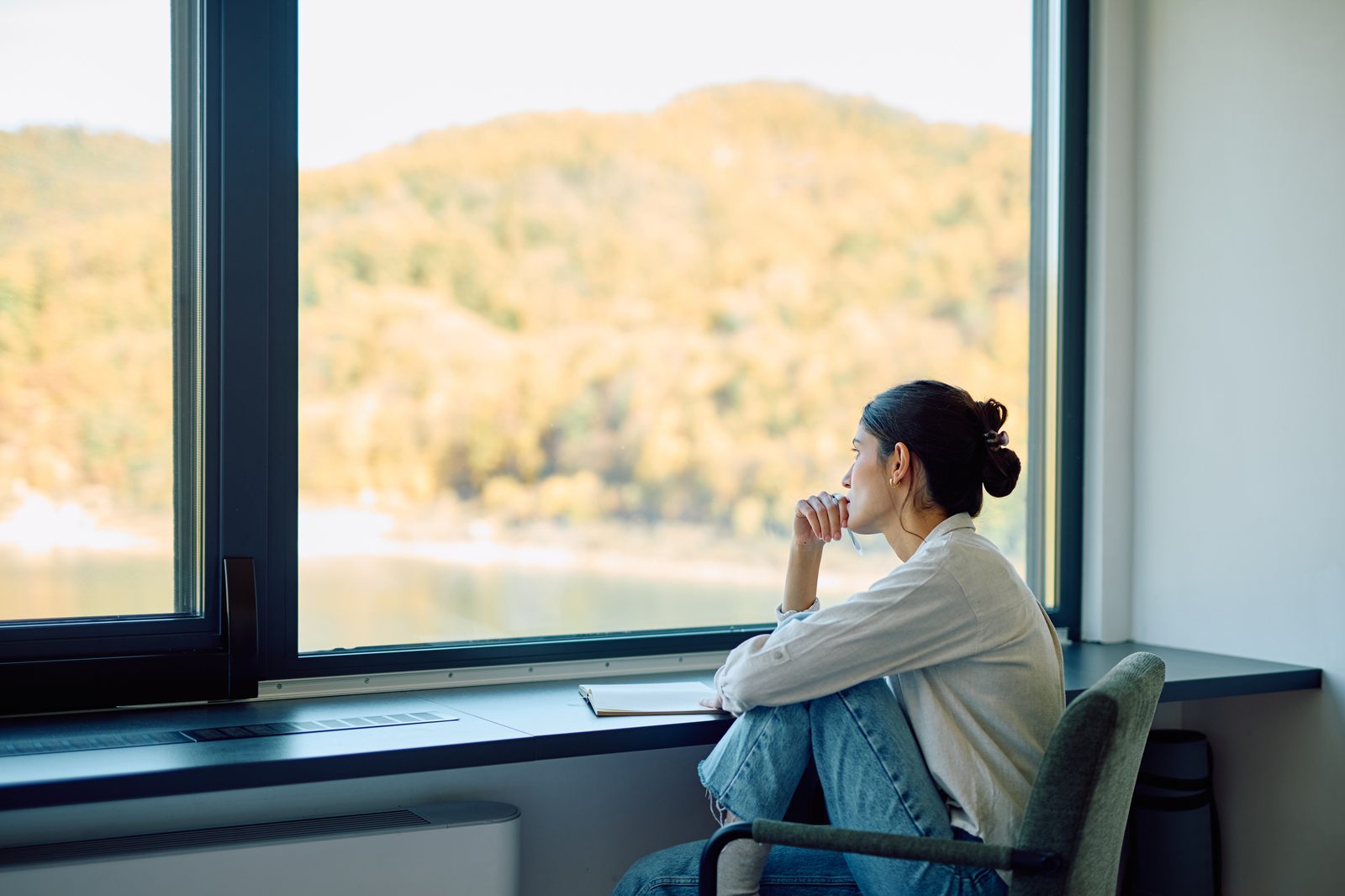 A woman sitting in a chair looking thoughtfully out of a window